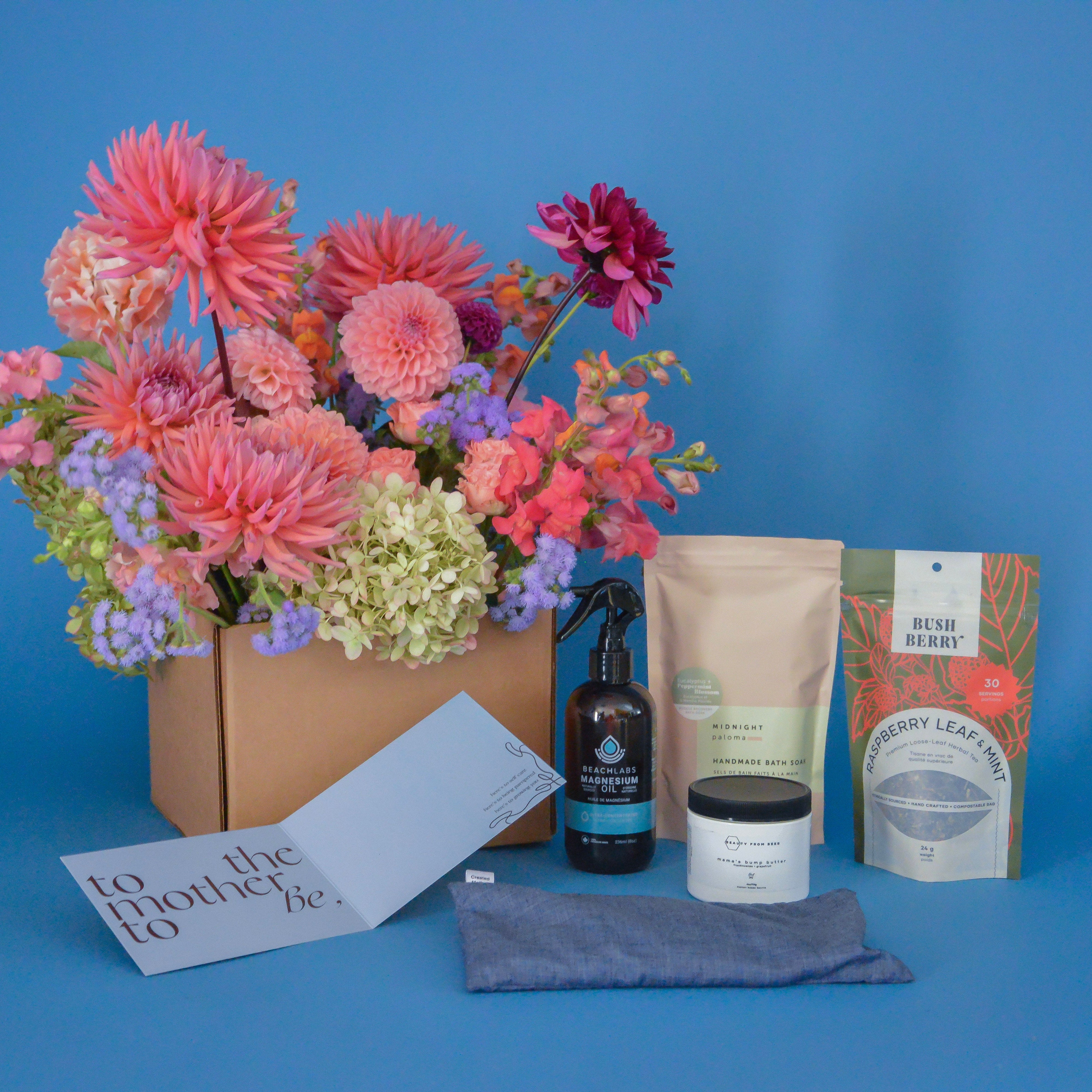 Gifting set with flowers, skincare products, and a card on a blue background